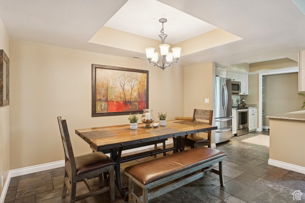 Dining space featuring stone tile floors, a chandelier, and a tray ceiling