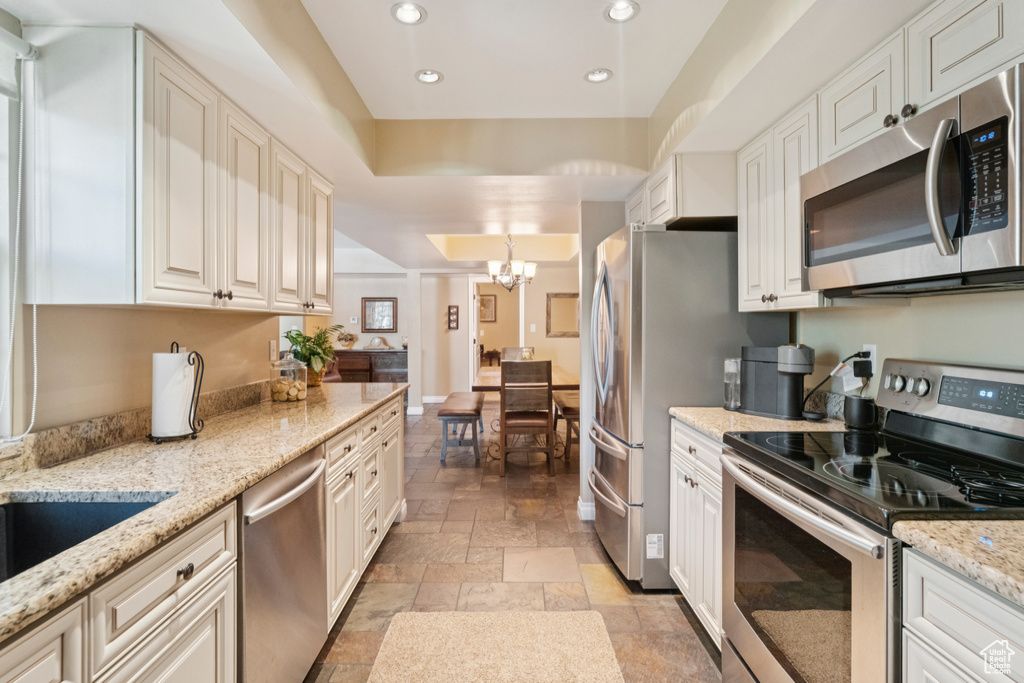Kitchen with stainless steel appliances, stone tile flooring, recessed lighting, a chandelier, and light stone countertops