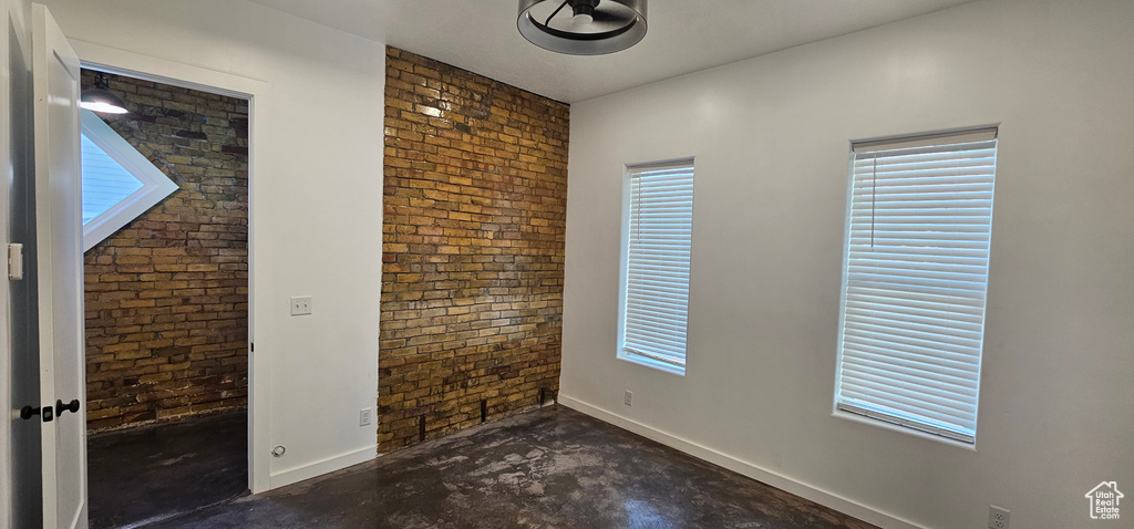 Empty room with unfinished concrete floors, brick wall, and plenty of natural light