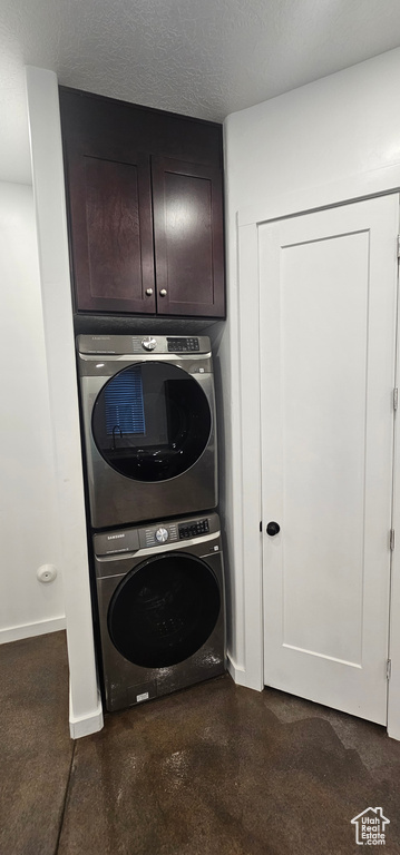 Washroom featuring stacked washer and clothes dryer, a textured ceiling, and cabinet space