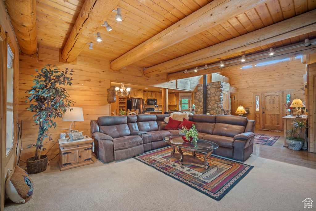 Carpeted living area with rail lighting, wooden walls, a chandelier, and a wood ceiling with exposed beams