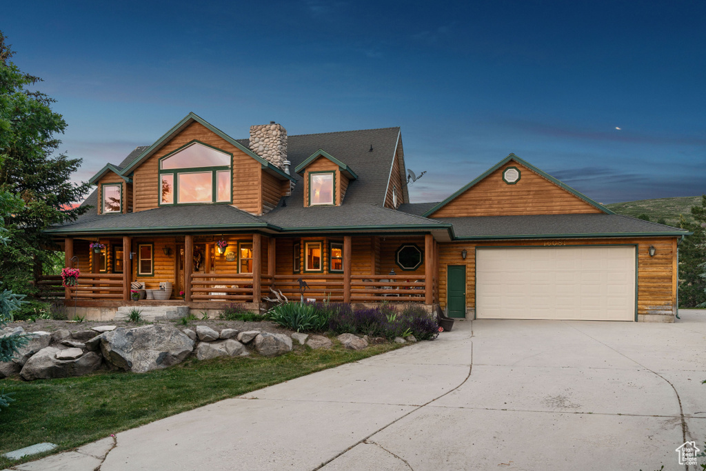 View of front of house featuring a porch, an attached garage, driveway, and a chimney