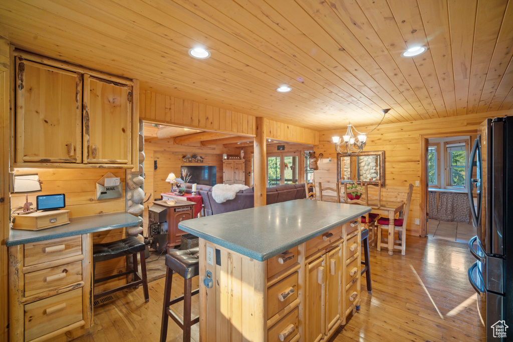 Kitchen featuring freestanding refrigerator, a breakfast bar area, wood walls, recessed lighting, and a chandelier