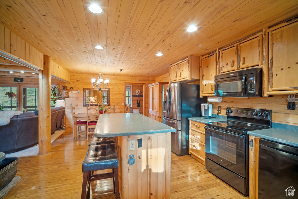 Kitchen with black appliances, a kitchen island, a chandelier, light wood-style flooring, and recessed lighting