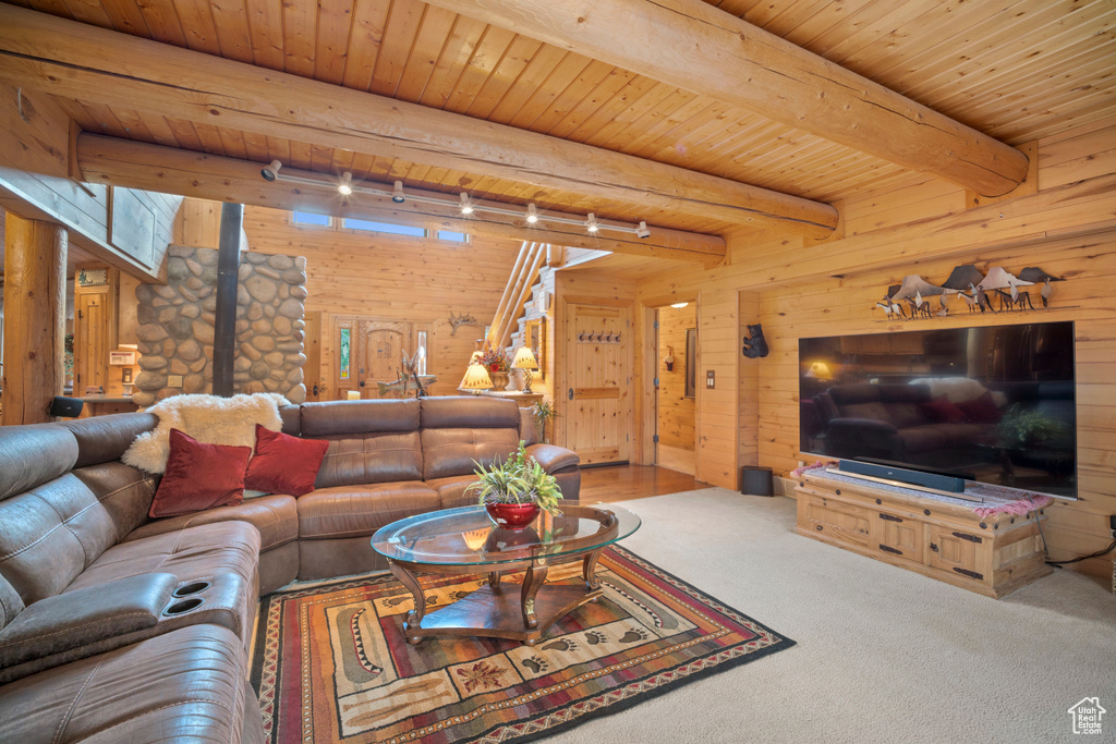 Living area featuring a wood ceiling with exposed beams, wooden walls, a wood stove, and carpet