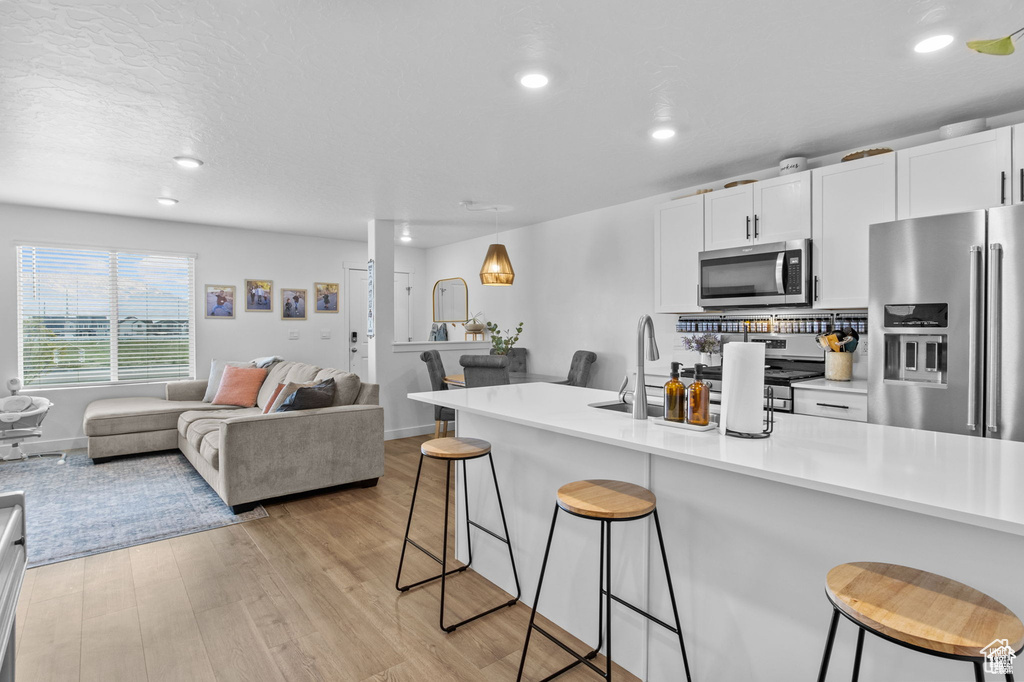 Kitchen featuring stainless steel appliances, a kitchen breakfast bar, open floor plan, light wood-type flooring, and recessed lighting