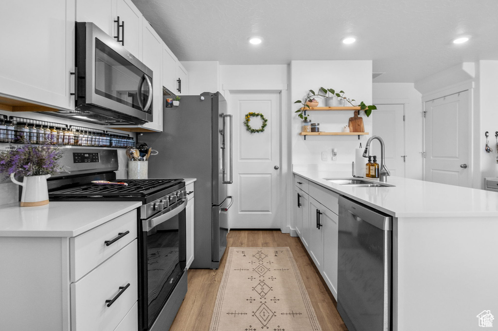 Kitchen featuring appliances with stainless steel finishes, open shelves, a peninsula, light wood-type flooring, and light countertops