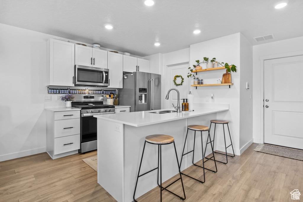 Kitchen featuring appliances with stainless steel finishes, a kitchen breakfast bar, open shelves, a peninsula, and light wood finished floors