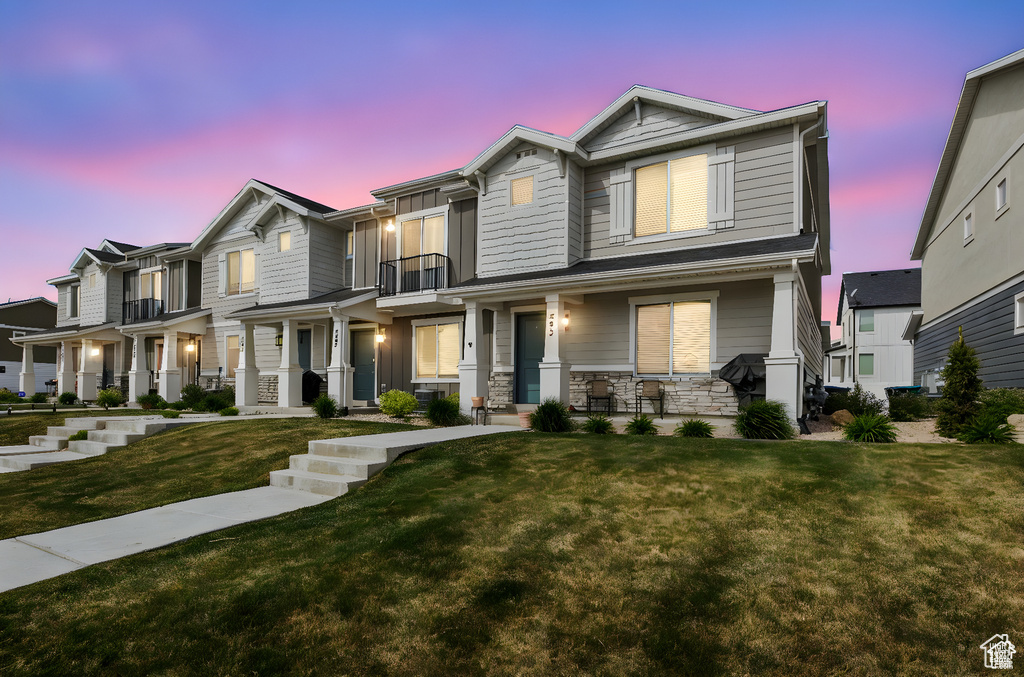 View of front of house featuring a balcony, a porch, a lawn, and stone siding
