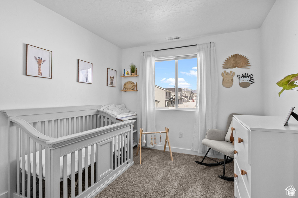 Carpeted bedroom featuring a nursery area and a textured ceiling