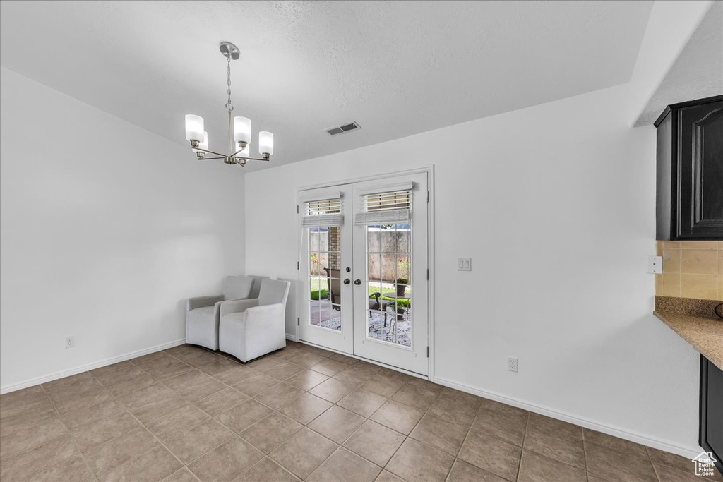 Unfurnished dining area with french doors, a chandelier, and light tile patterned flooring