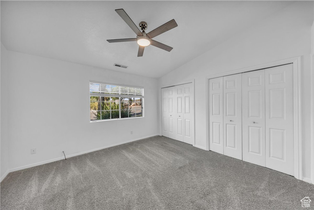 Unfurnished bedroom featuring two closets, carpet flooring, lofted ceiling, and ceiling fan