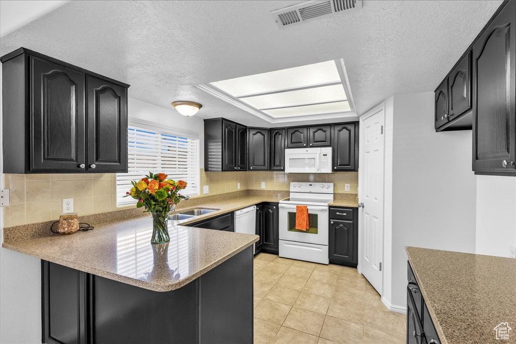 Kitchen with white appliances, tasteful backsplash, a peninsula, a textured ceiling, and light countertops