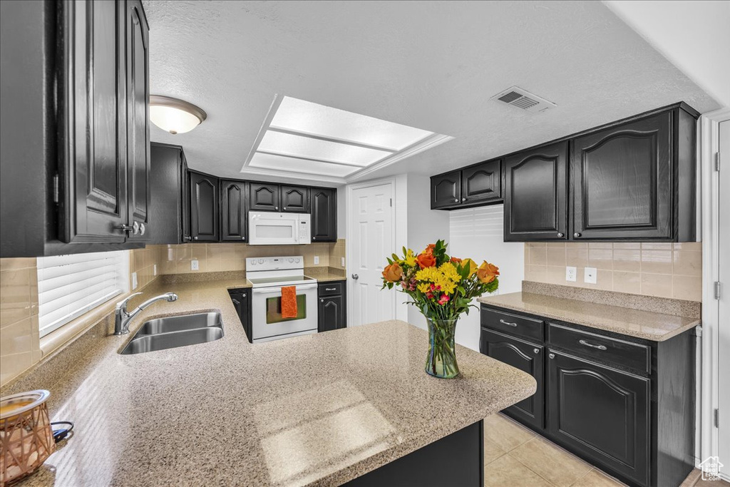 Kitchen featuring white appliances, dark cabinetry, backsplash, and a peninsula