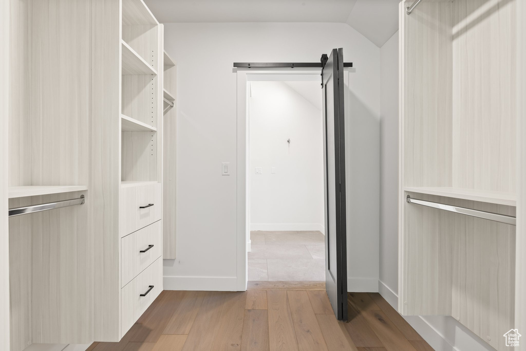 Walk in closet with light wood finished floors, a barn door, and lofted ceiling