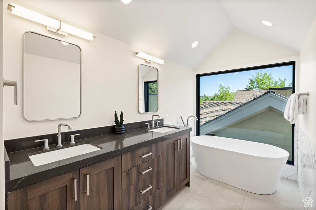 Full bathroom featuring double vanity, a freestanding bath, lofted ceiling, recessed lighting, and tile patterned floors