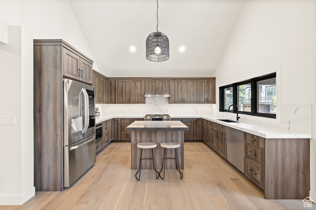 Kitchen with stainless steel appliances, a center island, a kitchen breakfast bar, high vaulted ceiling, and decorative backsplash