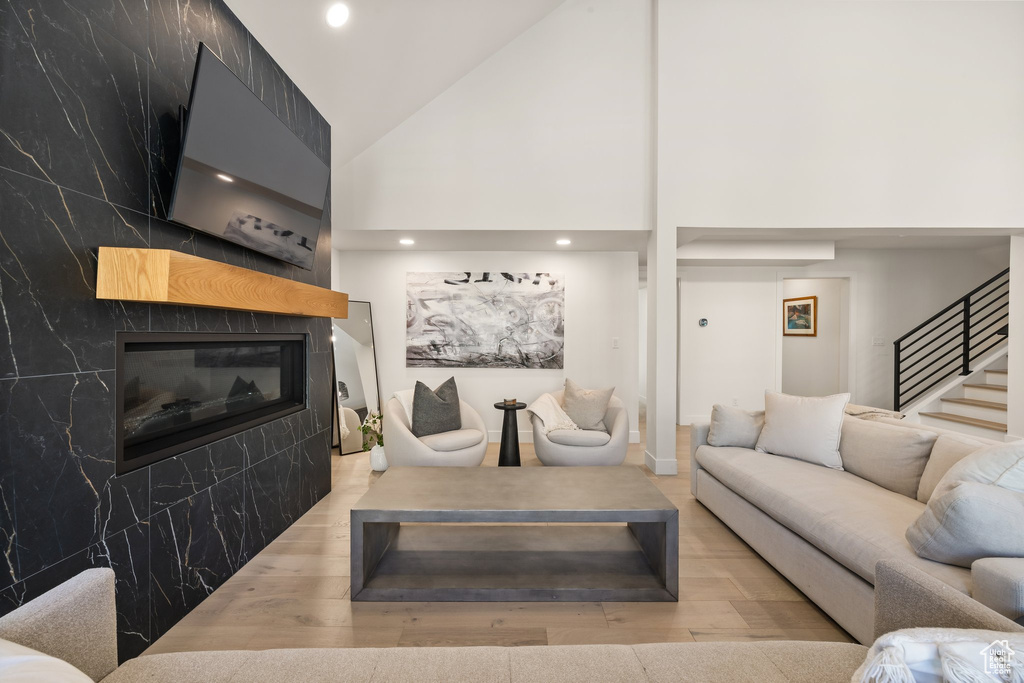 Living room featuring wood finished floors, a tile fireplace, high vaulted ceiling, stairway, and recessed lighting