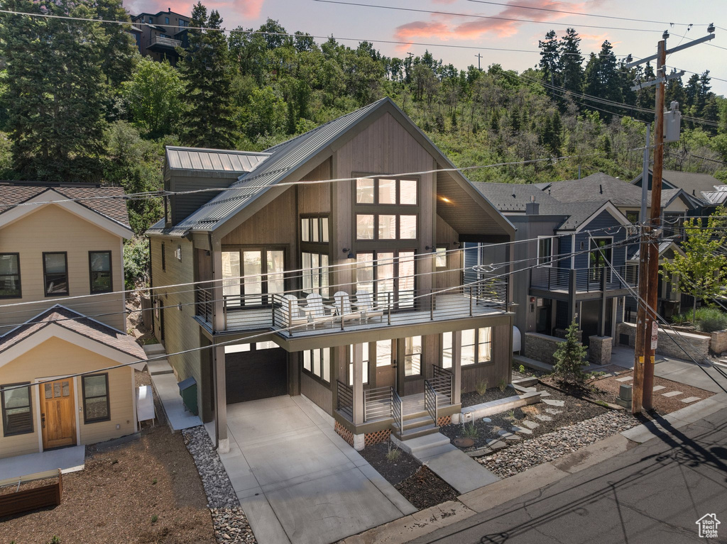 Rear view of property with a balcony, driveway, a metal roof, and a garage