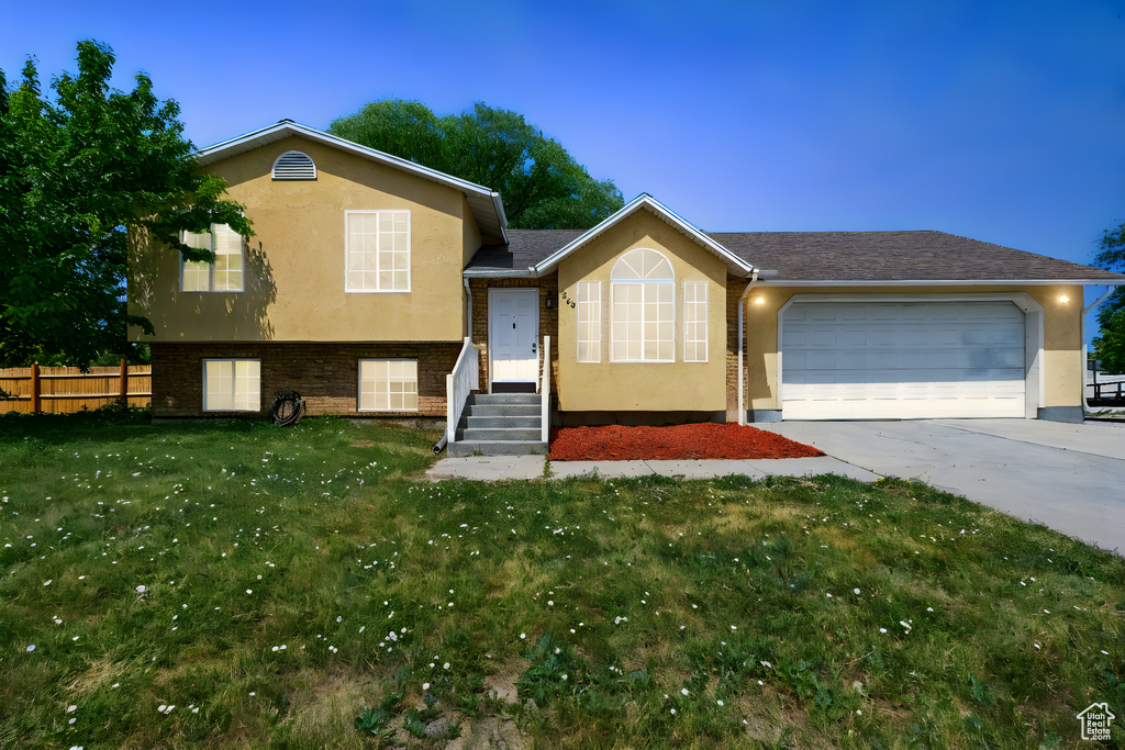 Tri-level home featuring stucco siding, a garage, concrete driveway, and brick siding