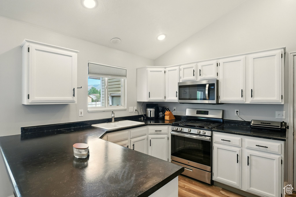 Kitchen with appliances with stainless steel finishes, vaulted ceiling, white cabinets, and recessed lighting