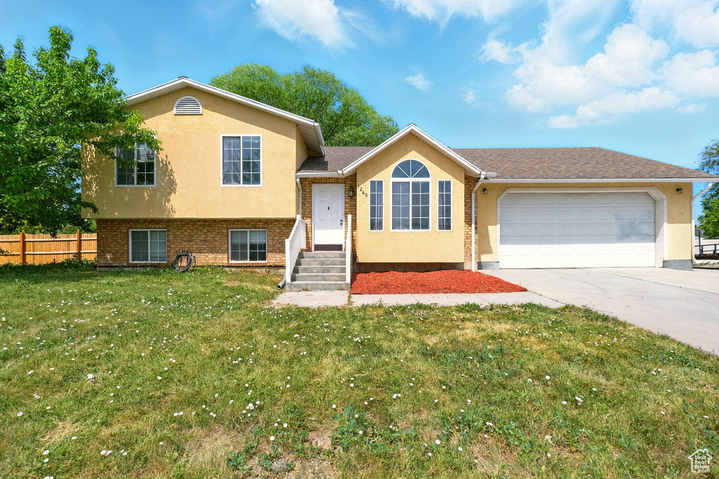 Split level home with stucco siding, an attached garage, and driveway