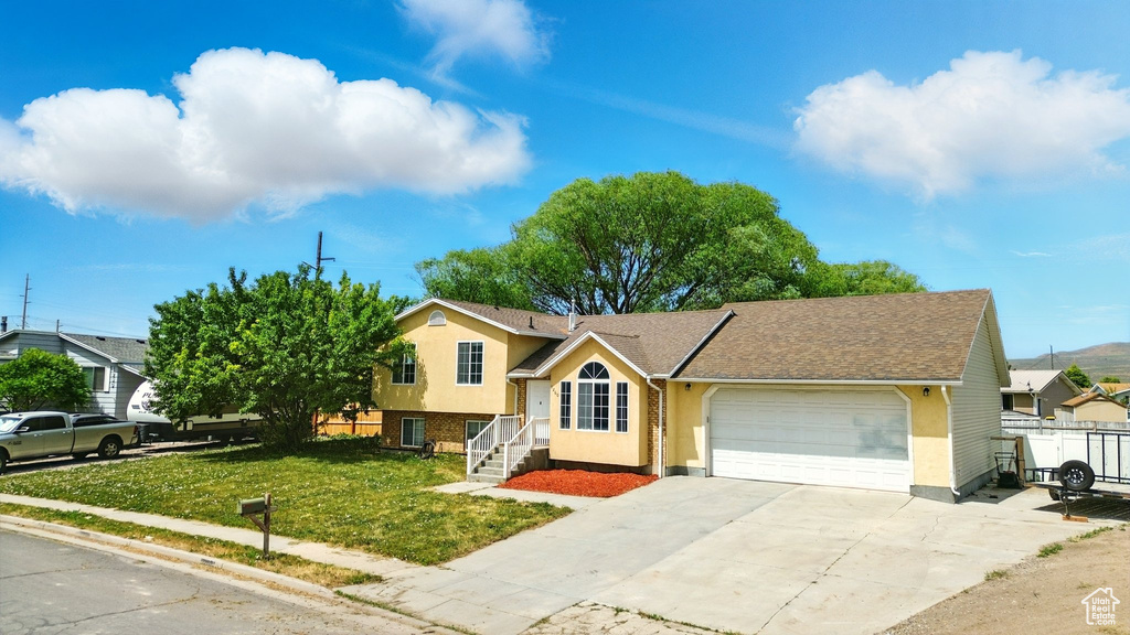 Split level home with a garage, concrete driveway, and stucco siding