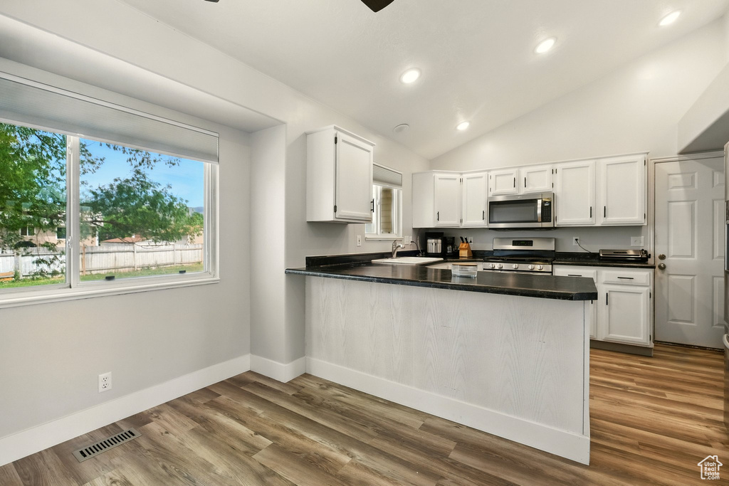 Kitchen with stainless steel appliances, a peninsula, white cabinetry, dark countertops, and recessed lighting