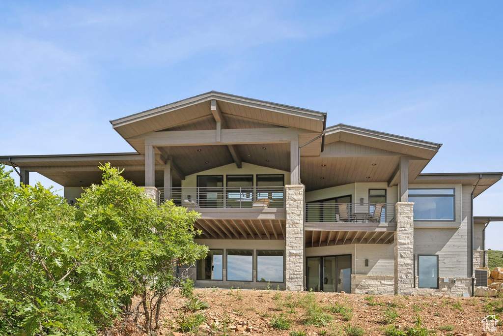 Rear view of property featuring a balcony and stone siding
