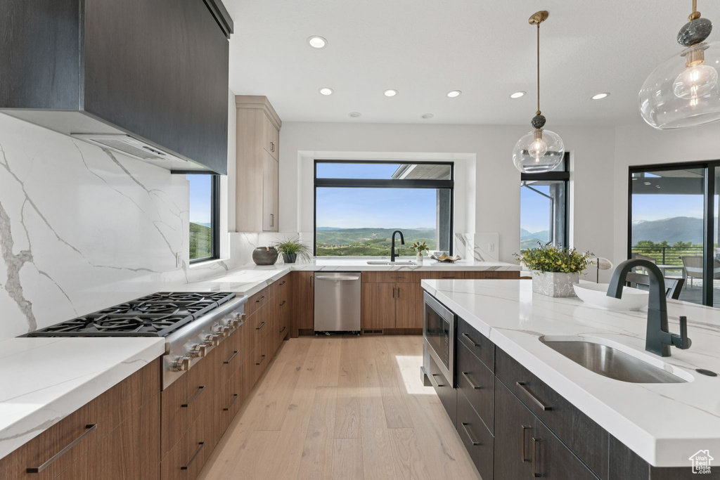 Kitchen with appliances with stainless steel finishes, light wood-type flooring, recessed lighting, light stone counters, and backsplash