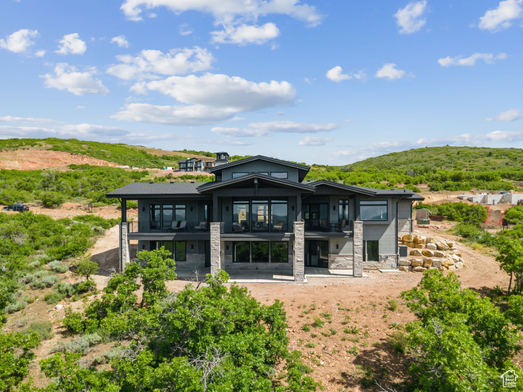 Back of property featuring a balcony, a patio, a mountain view, and stone siding