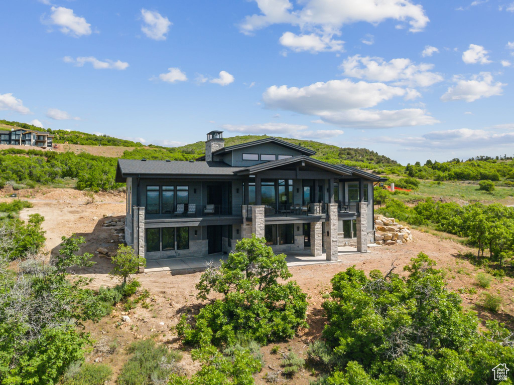 Rear view of property featuring a balcony, a patio, stone siding, and a chimney