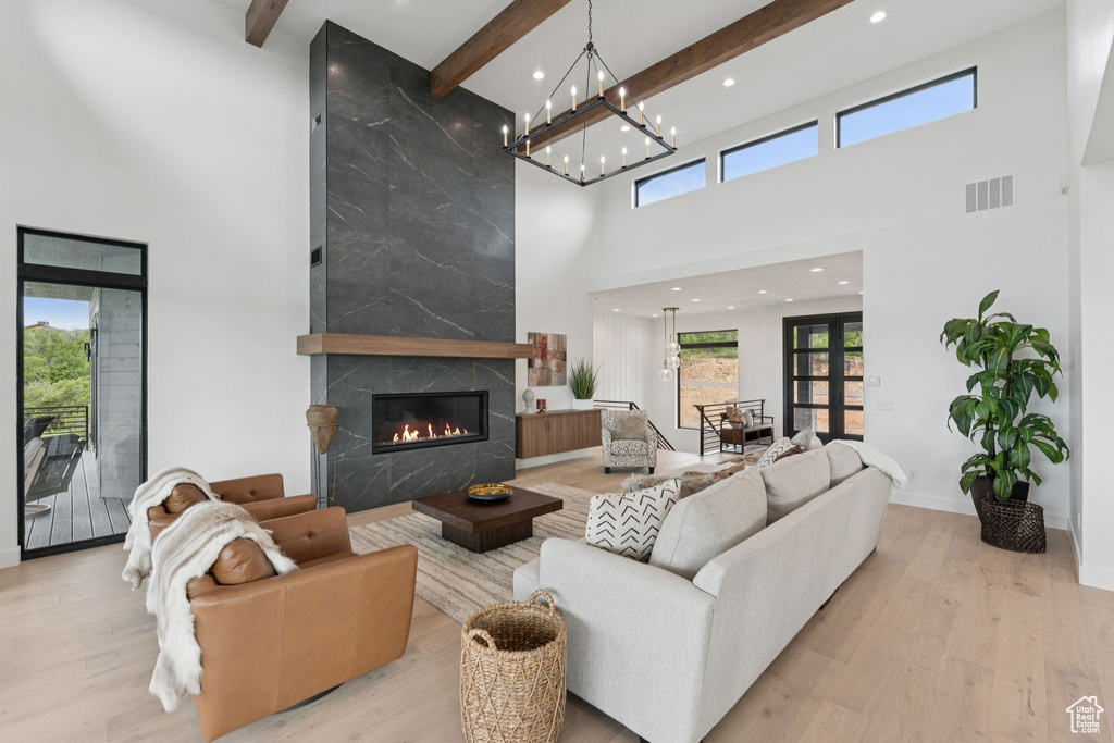 Living area with a towering ceiling, beamed ceiling, a premium fireplace, wood finished floors, and a chandelier