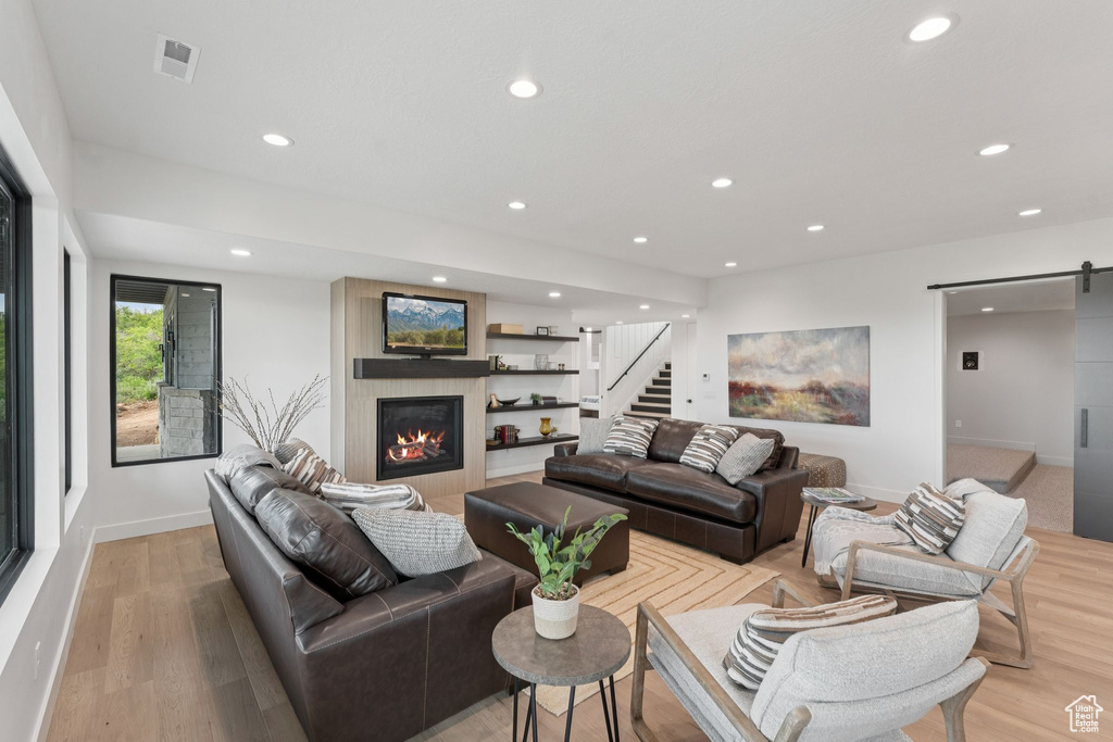 Living area with a barn door, a large fireplace, stairs, recessed lighting, and light wood-style floors