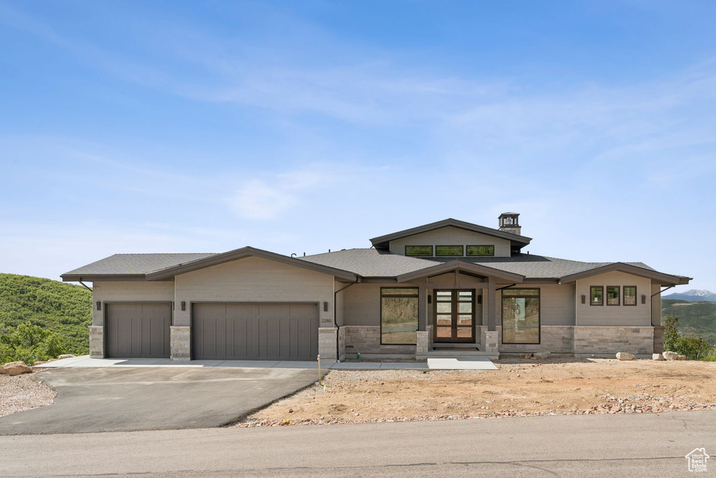 View of front of property with a garage, stone siding, driveway, a chimney, and roof with shingles