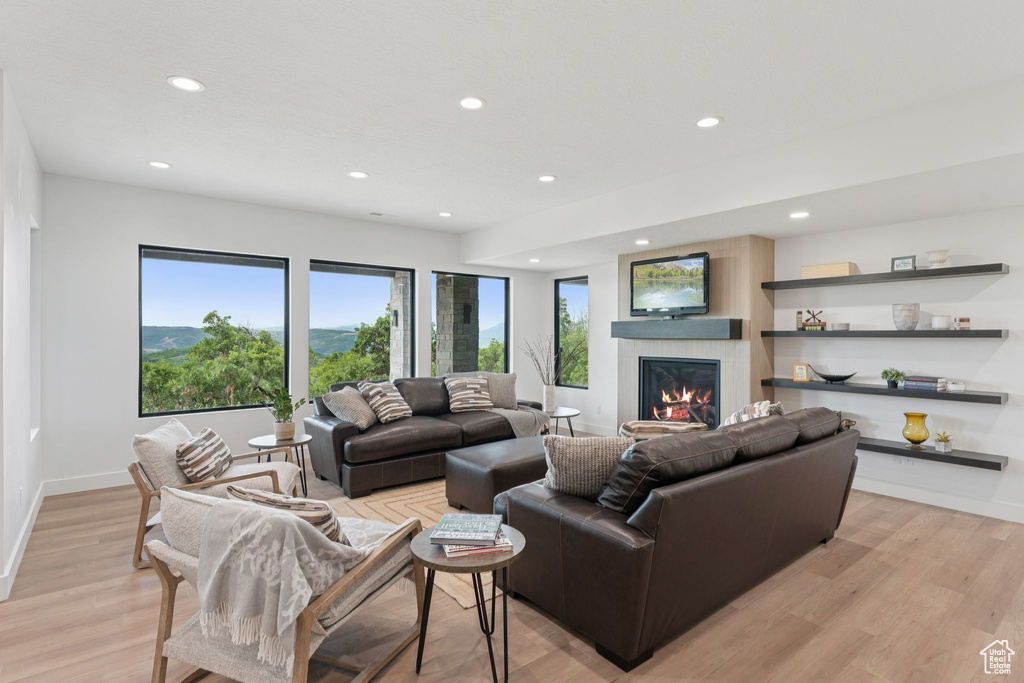 Living room featuring recessed lighting, a warm lit fireplace, and light wood-type flooring