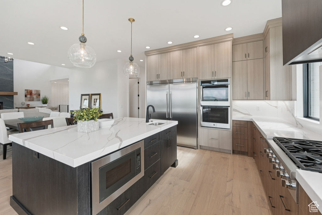 Kitchen featuring built in appliances, light wood finished floors, recessed lighting, light brown cabinetry, and a kitchen island with sink