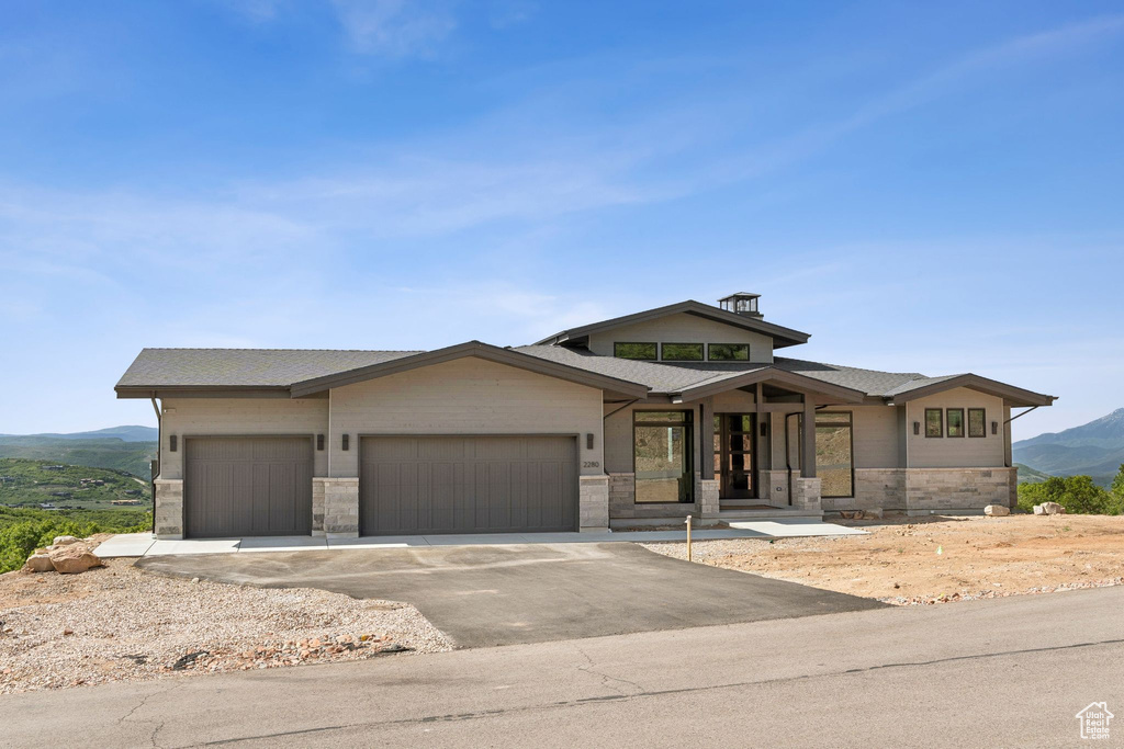 View of front of property with a garage, a mountain view, driveway, stone siding, and a shingled roof