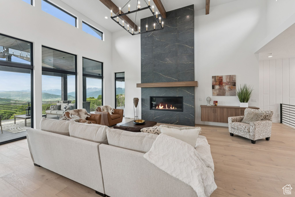 Living room featuring a towering ceiling, a premium fireplace, a chandelier, beamed ceiling, and wood finished floors