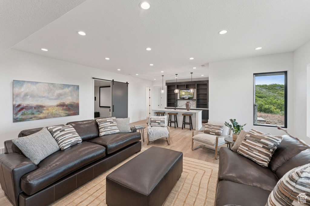Living area with a barn door, light wood finished floors, and recessed lighting