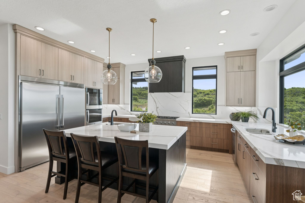 Kitchen featuring appliances with stainless steel finishes, light stone countertops, light wood-style flooring, decorative backsplash, and recessed lighting