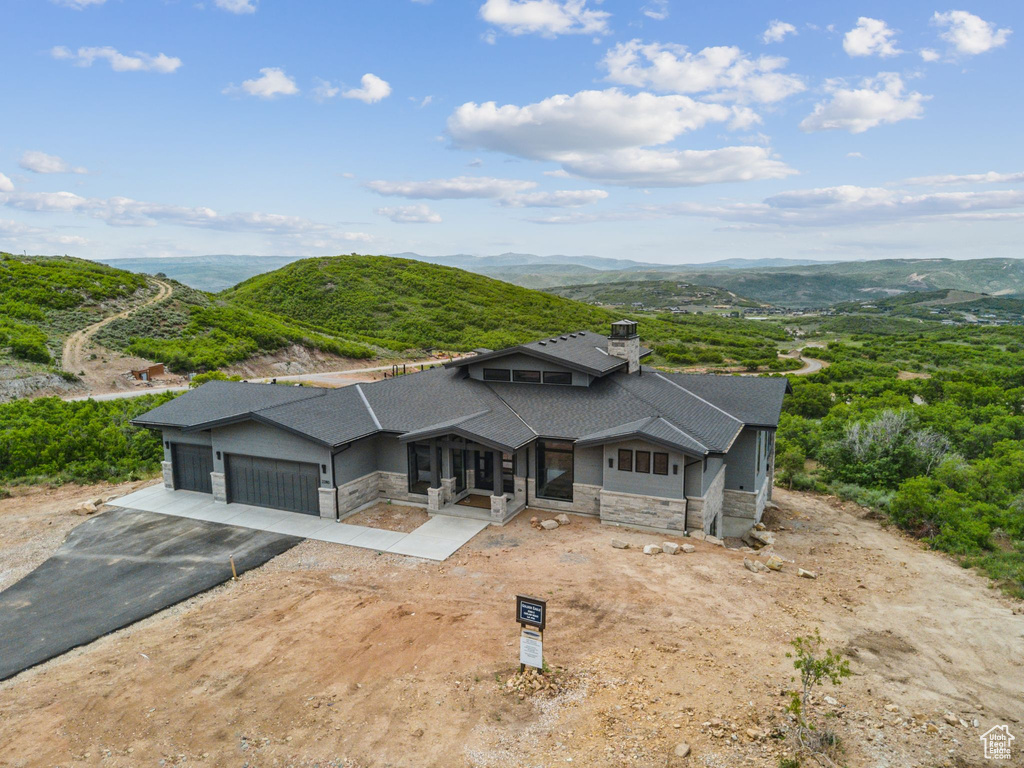 View of front of house with stone siding, a garage, roof with shingles, and a mountain view