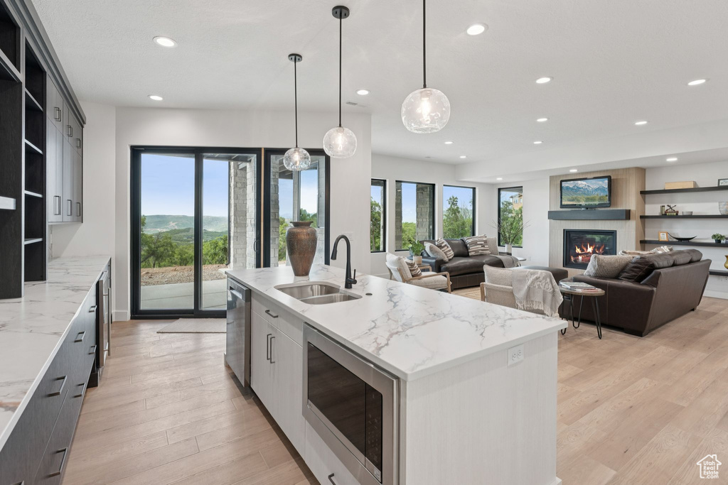 Kitchen featuring open shelves, stainless steel appliances, recessed lighting, an island with sink, and light wood finished floors