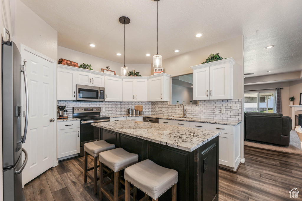 Kitchen with appliances with stainless steel finishes, white cabinetry, a center island, dark wood finished floors, and decorative backsplash