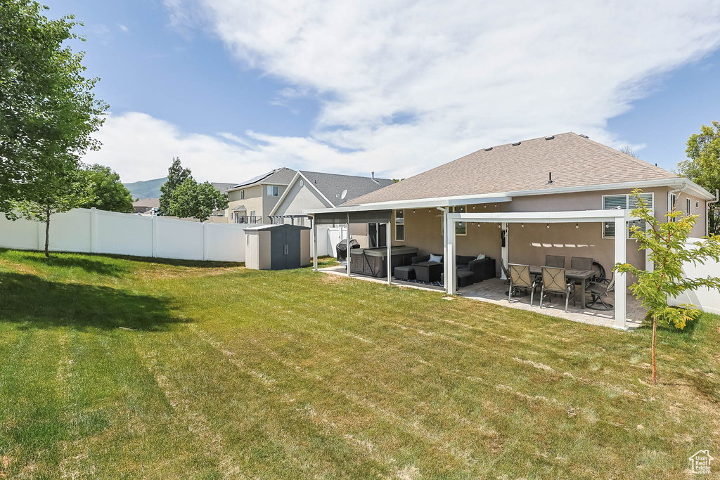 Back of house with outdoor lounge area, a shed, a patio area, a fenced backyard, and roof with shingles