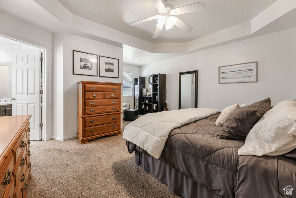 Bedroom with light carpet, a tray ceiling, and a ceiling fan
