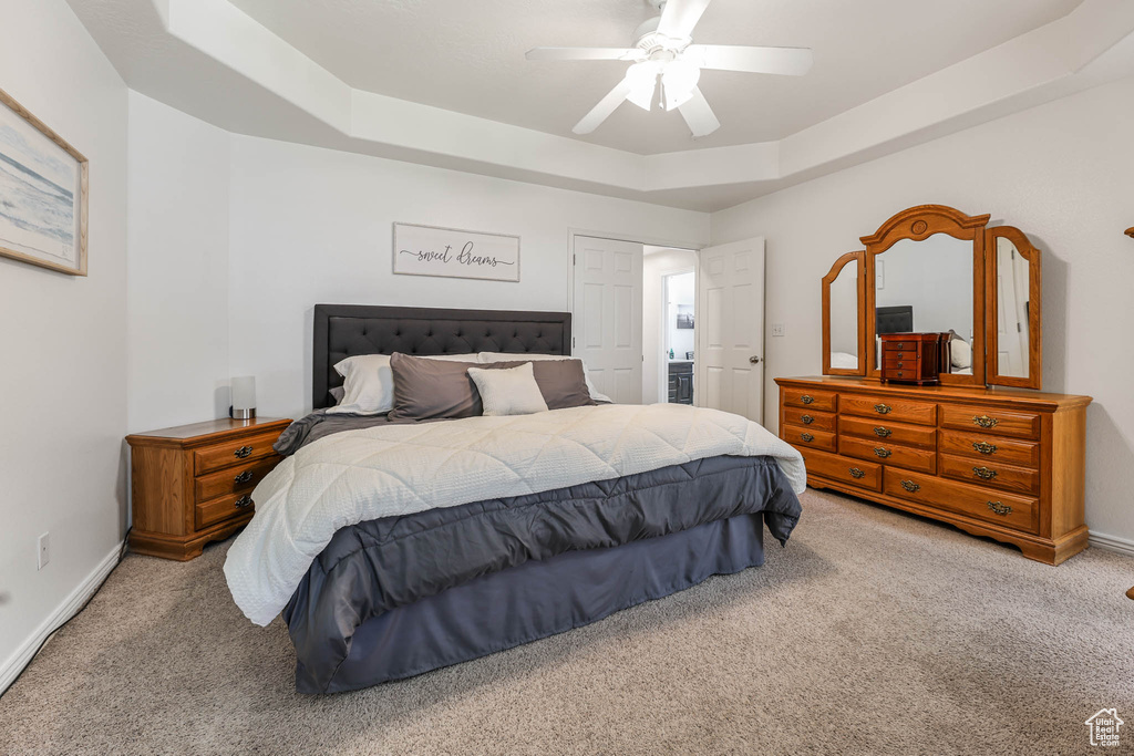 Carpeted bedroom featuring a tray ceiling and a ceiling fan