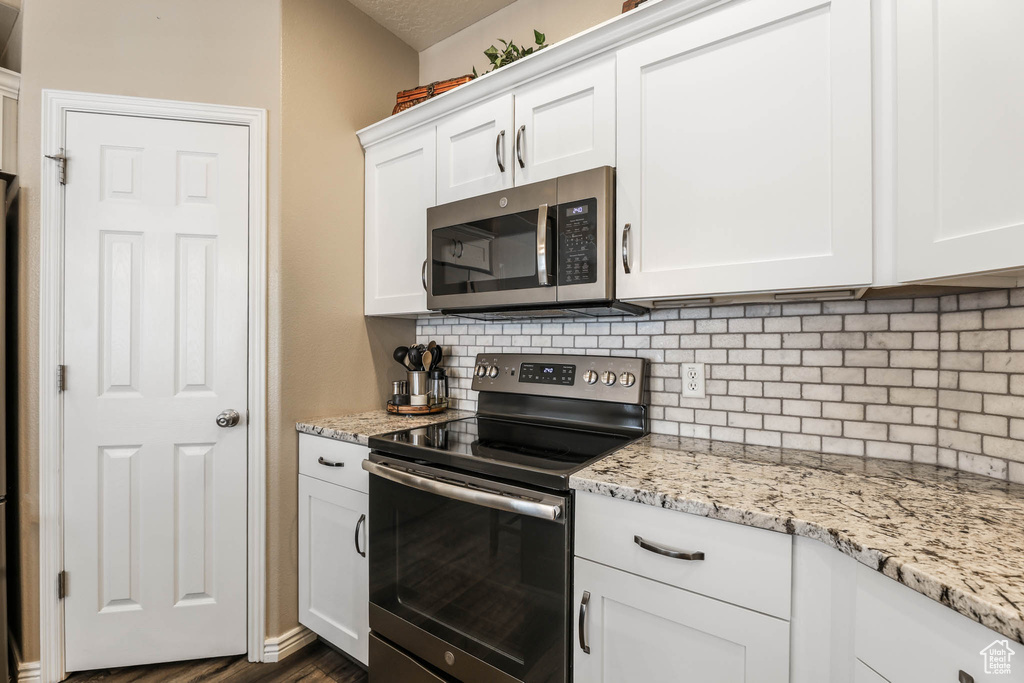 Kitchen featuring stainless steel appliances, backsplash, white cabinetry, and light stone countertops