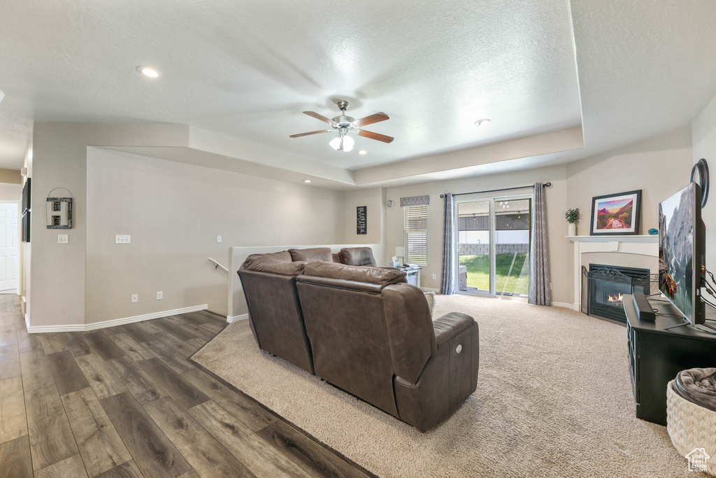 Living area featuring a tray ceiling, a ceiling fan, a glass covered fireplace, dark wood-type flooring, and recessed lighting