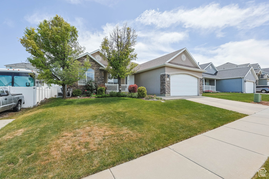 View of front of home with stone siding, a front lawn, a garage, and driveway